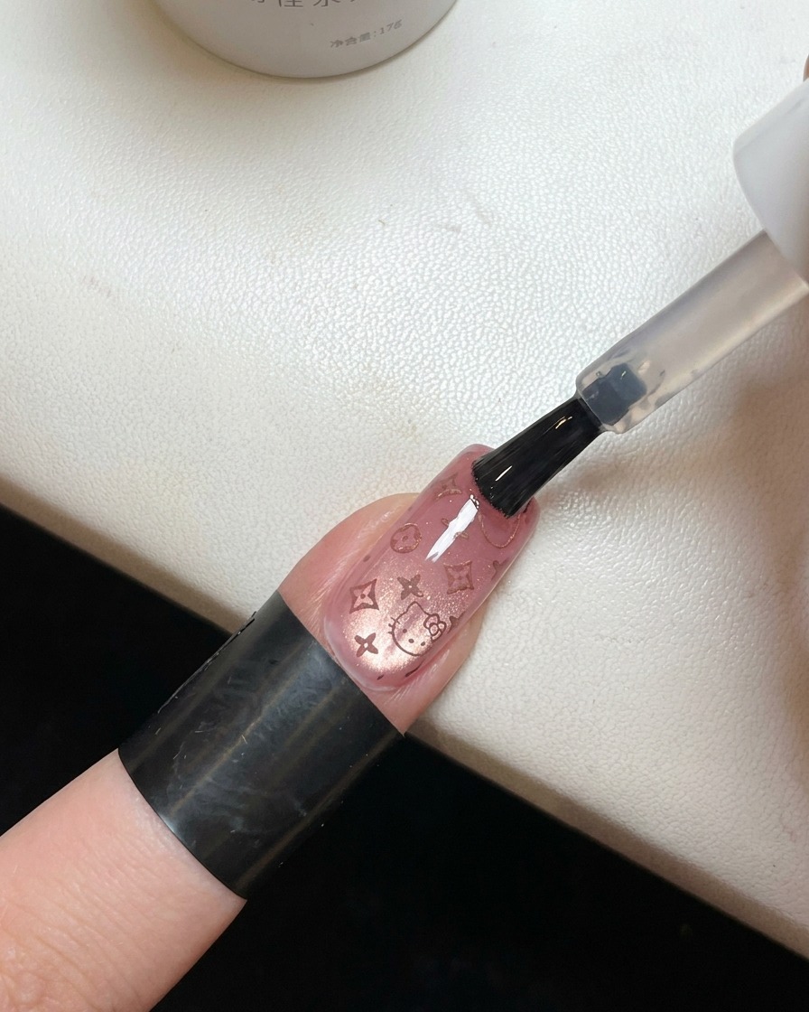 Pędzelek aplikujący bezbarwny, błyszczący top coat na paznokieć z różowym wzorem Hello Kitty.