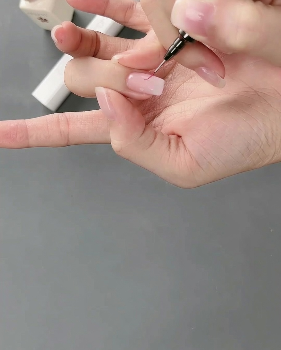 Zbliżenie na cienki pędzelek typu liner rysujący detale wokół krawędzi różowego bloku żelu.