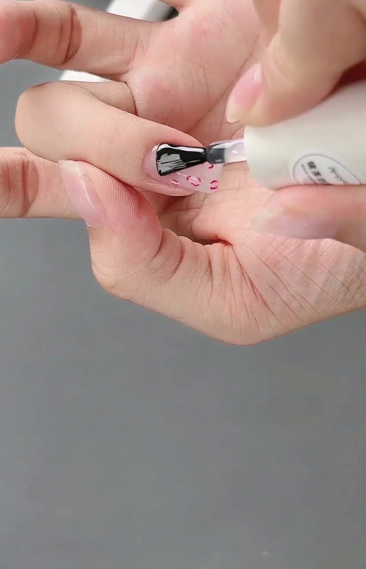 Pędzelek nakładający błyszczący top coat na gotowy wzór z kokardką 3D.