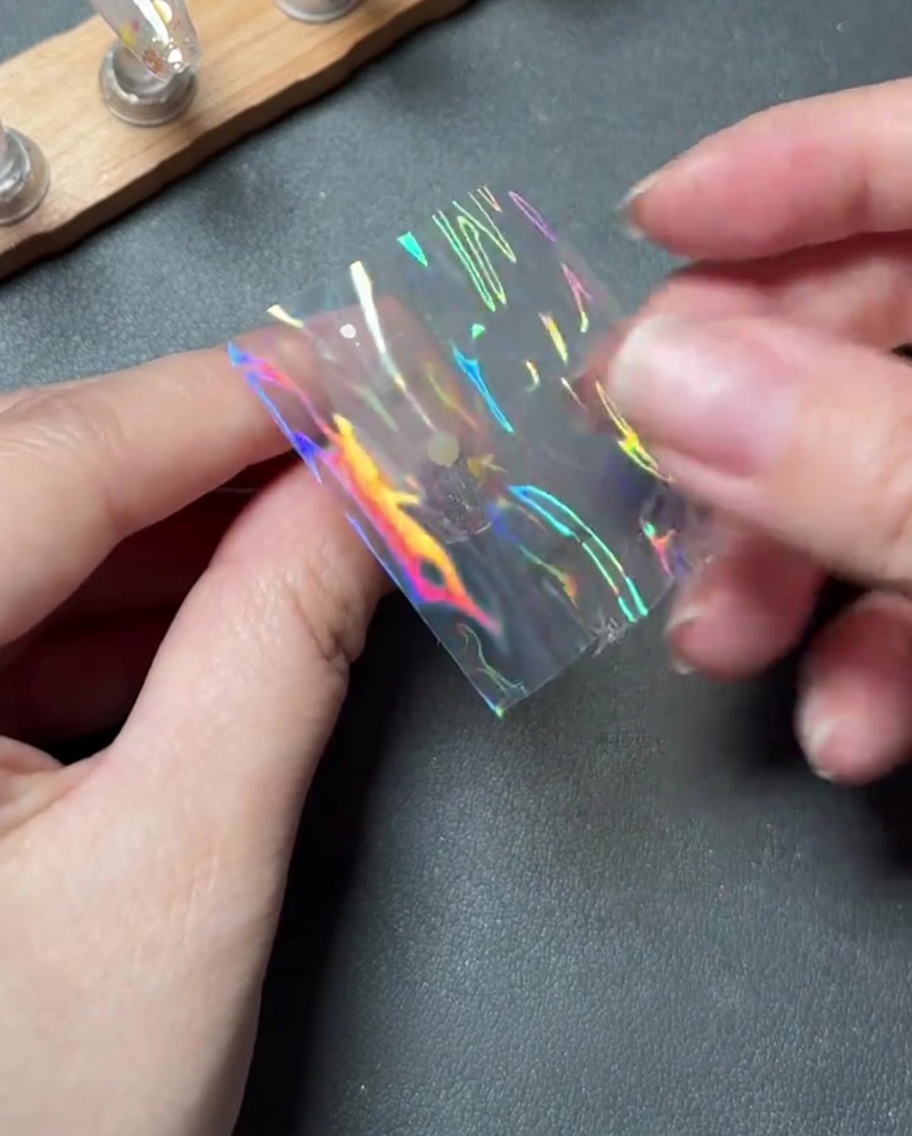 Palce ostrożnie umieszczające mały kawałek holograficznej folii na środku paznokcia.