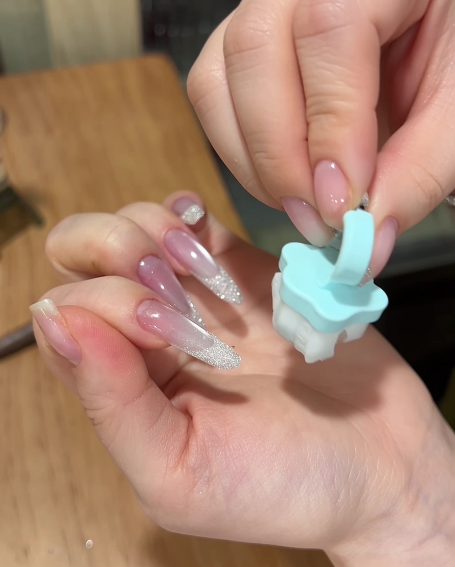 Dłoń używająca małego, miękkiego niebieskiego pędzelka do usunięcia nadmiaru pyłku z powierzchni gotowego manicure.