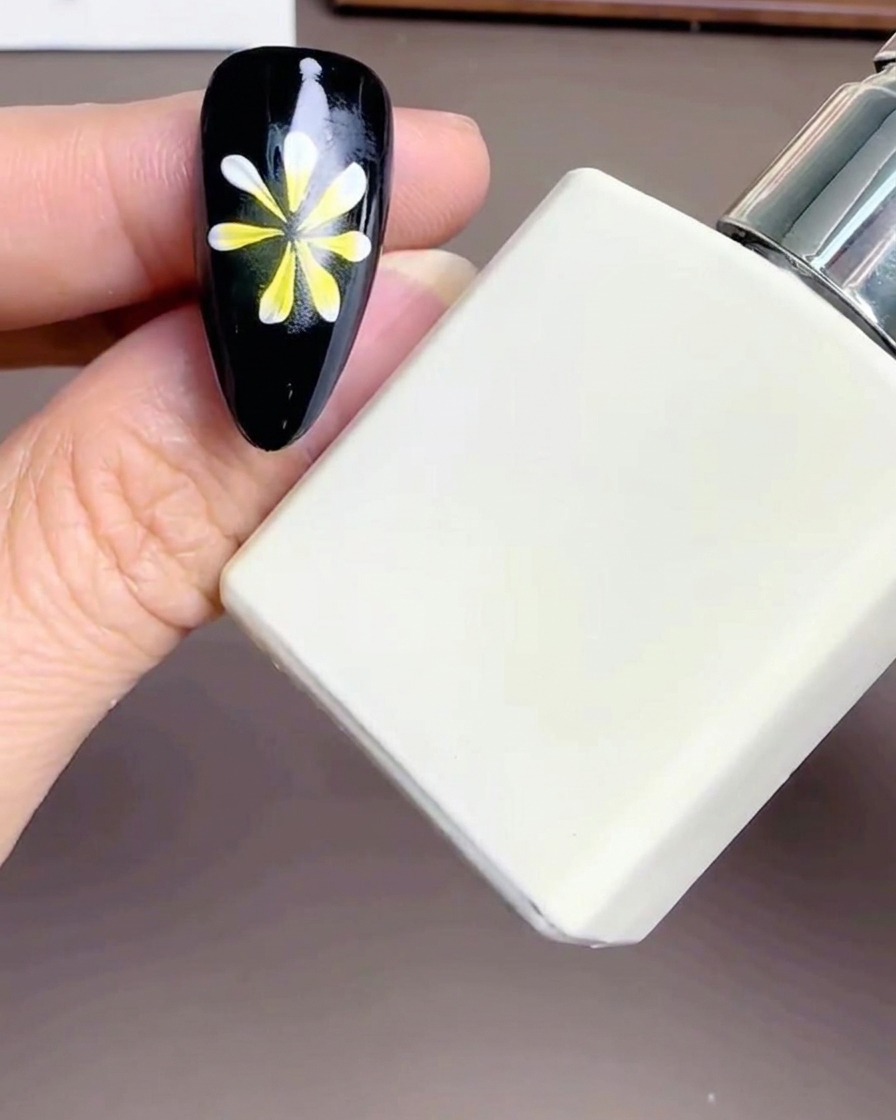Zbliżenie na buteleczkę Diamond Top Coat trzymaną obok paznokcia ze zdobieniem kwiatowym.