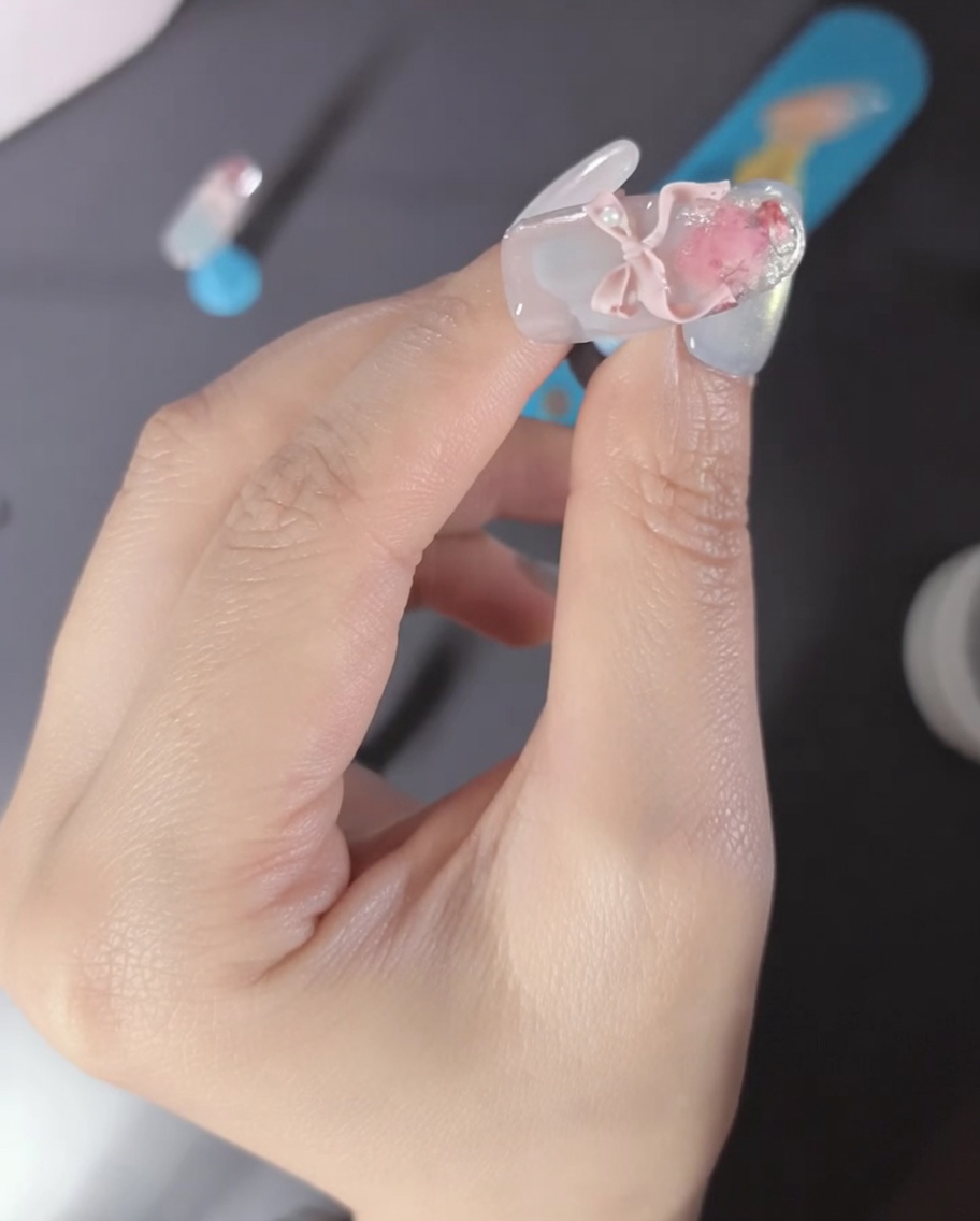 Zbliżenie palca z różową kokardką 3D i perłowymi akcentami.