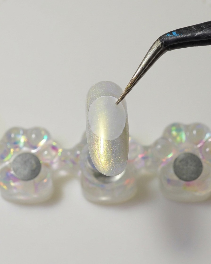 Metalowa szpatułka nakłada kropkę gęstego, bezbarwnego żelu budującego na spód plastikowego dysku.