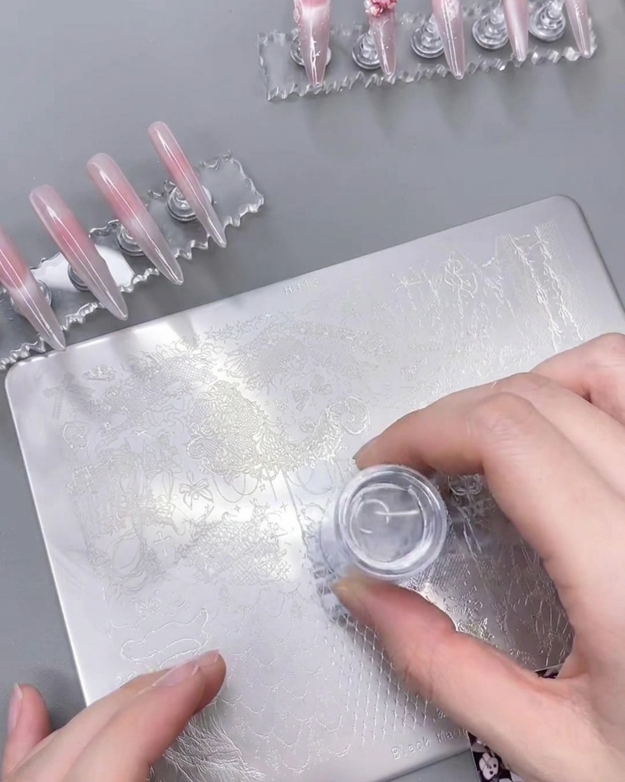 Przezroczysty silikonowy stempel do paznokci dociśnięty do stalowej płytki, na którym z sukcesem odbił się wzór białej koronki.