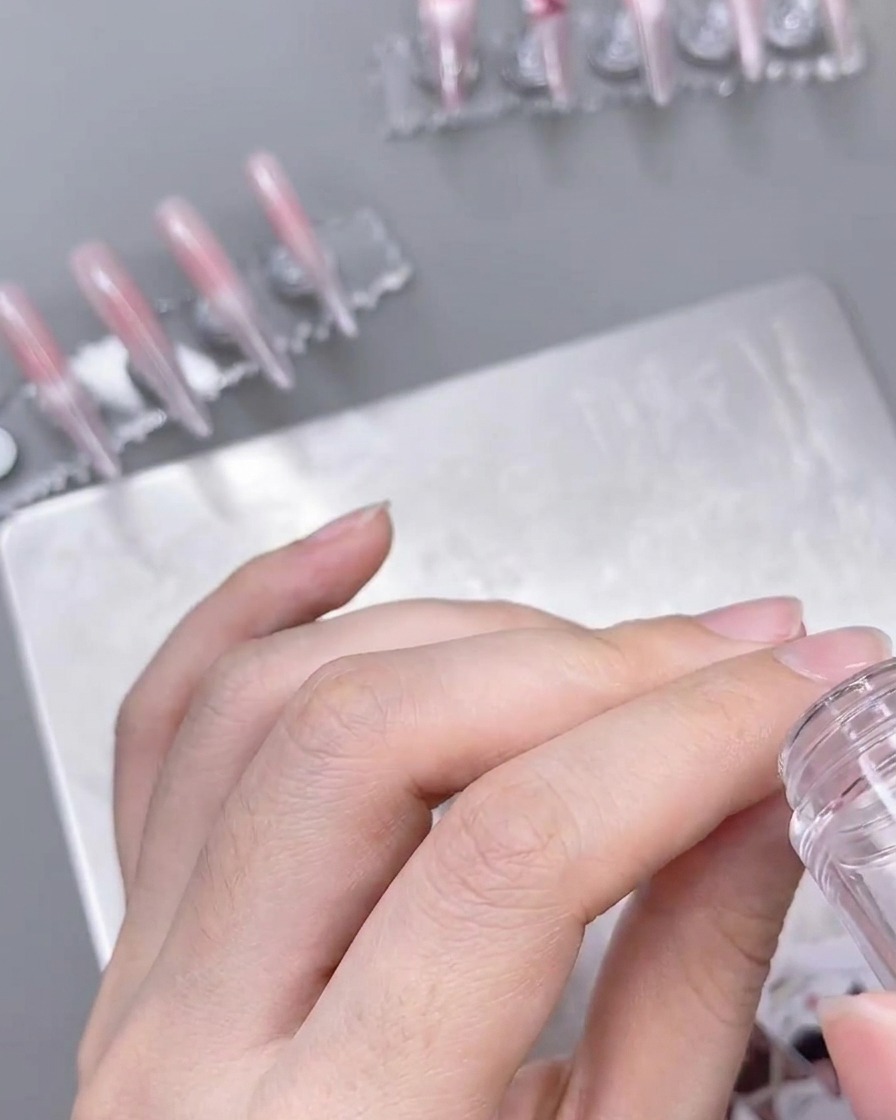 Przezroczysty stempel nanoszący delikatny wzór białej koronki na przygotowany paznokieć w kolorze ombre.
