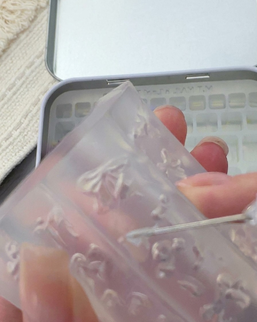 Narzędzie wyjmujące małą, delikatną białą kokardkę 3D z silikonowej formy.