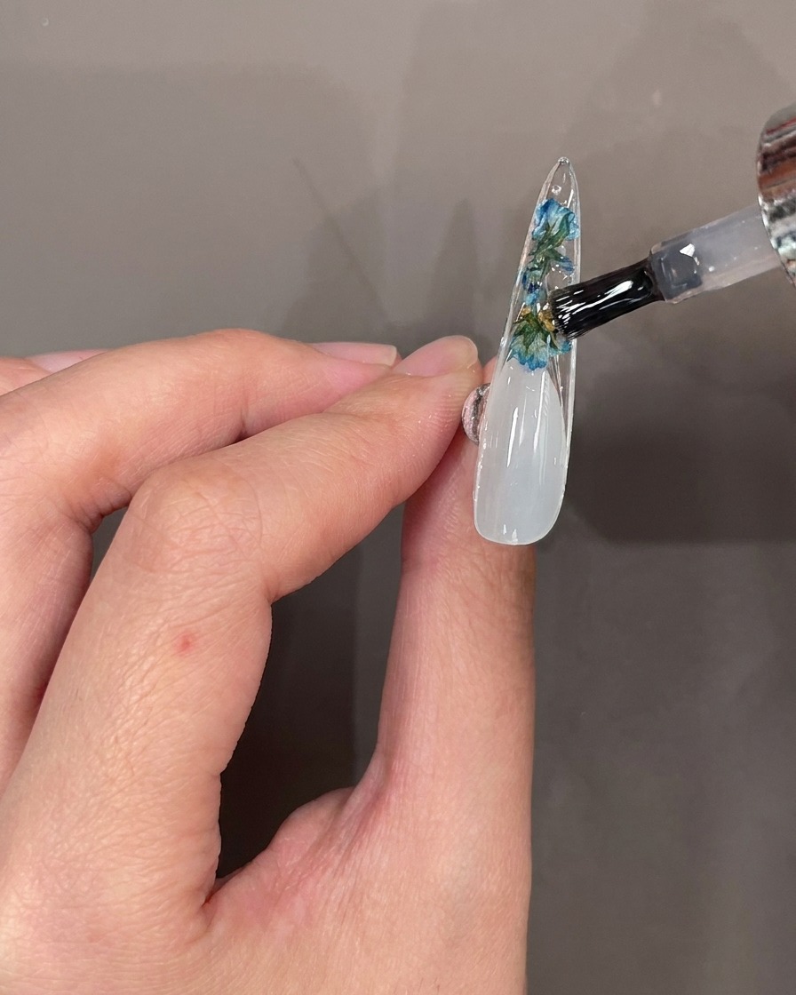 Pędzelek do paznokci nakładający przezroczysty top coat na kwiaty i cyrkonie na spodzie tipsa.