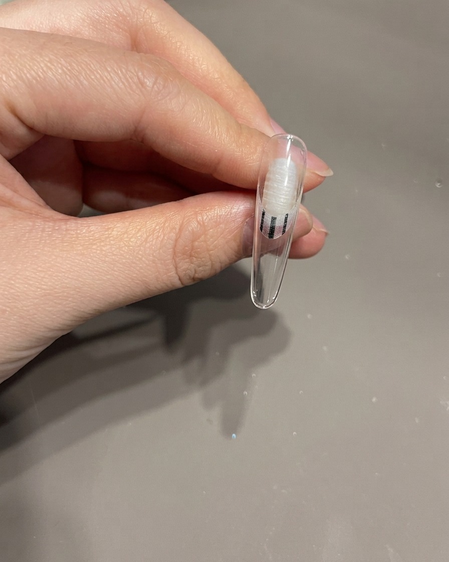 Zbliżenie na dłoń wkładającą paznokieć z kokardą 3D do lampy UV.