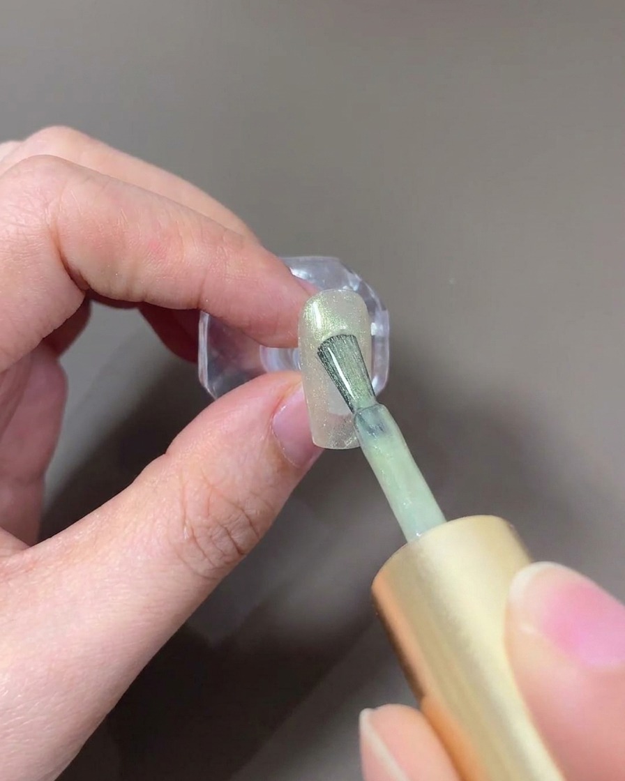 Pędzelek nakładający jasny żel cat-eye typu glass na płytkę paznokcia.