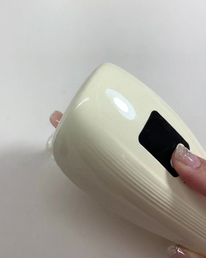 Ręka trzymająca małą lampę UV/LED nad pomalowanym paznokciem.