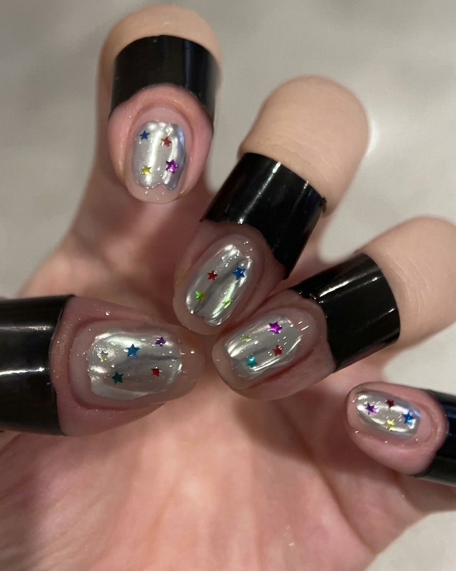 Pędzelek nakłada przezroczysty top coat na srebrny paznokieć chromowany.