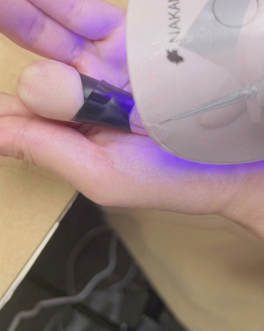 Paznokieć wkładany pod mini lampę UV/LED w celu utrwalenia zdobienia.