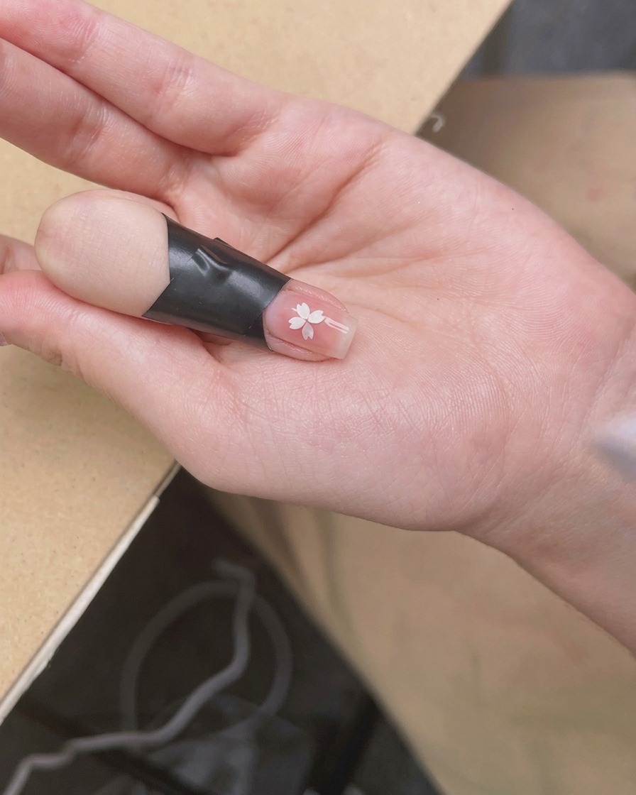 Dłoń pod mini lampą UV/LED podczas utwardzania kleju z ozdobą.