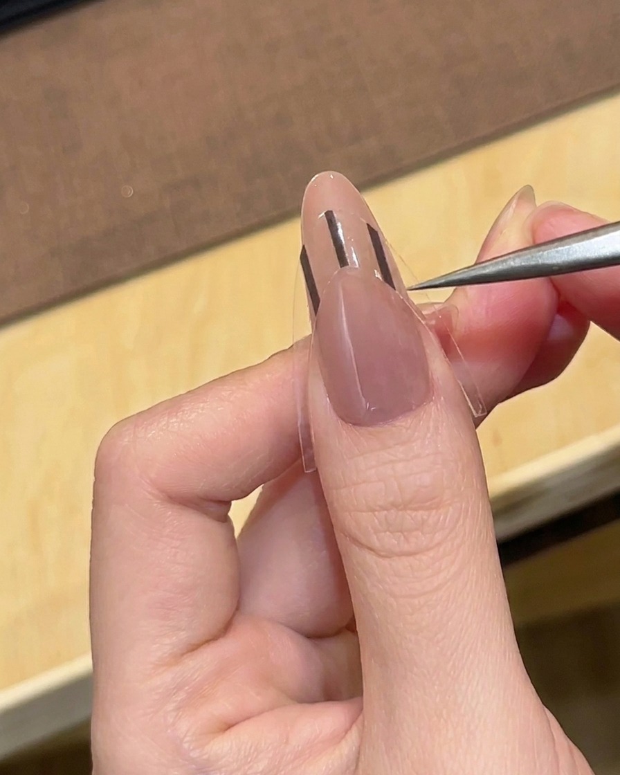 Pęseta umieszczająca czarną naklejkę do french manicure na pomalowanym paznokciu.