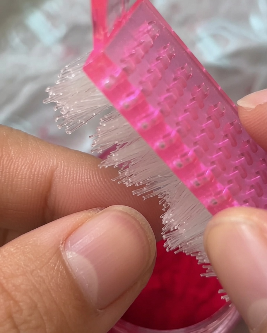 Zbliżenie na różowy pędzelek do manicure omiatający paznokieć pokryty czerwonym pluszem.