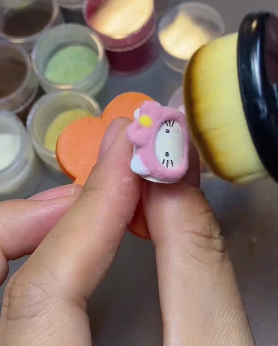 Zbliżenie na puszysty pędzel do makijażu zamiatający luźny różowy puder velvet z powierzchni charmsa Hello Kitty.