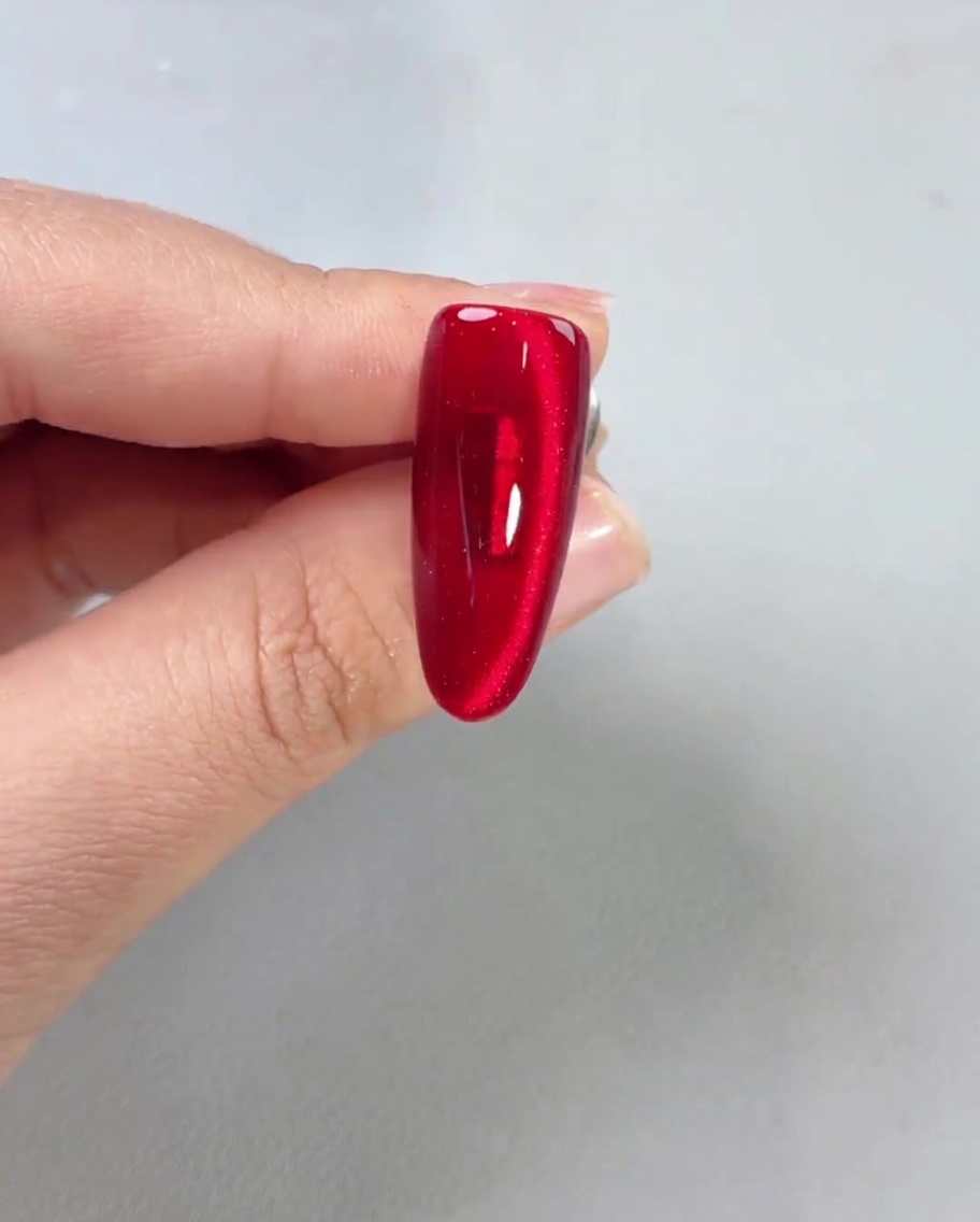 Błyszczący top coat nakładany na wykończony czerwony paznokieć magnetyczny, pokazujący wysoki połysk.