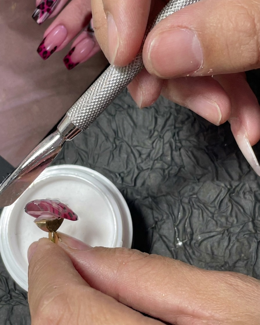 Narzędzie do manicure używane do posypywania drobnego białego proszku akrylowego na mokre czerwone kropki żelu na różowym paznokciu.
