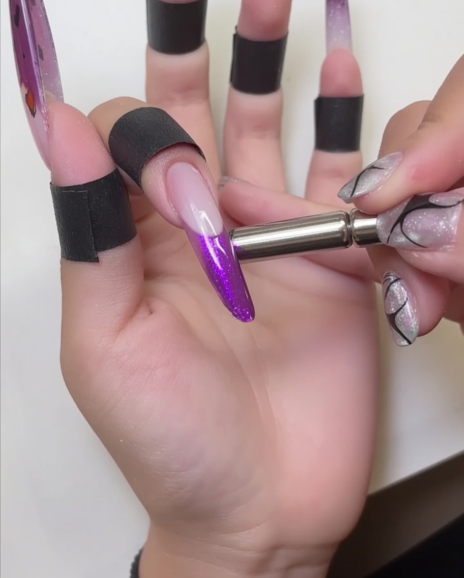 Metalowy magnes trzymany blisko końcówki paznokcia, wydobywający lśniący efekt w czerwonym lakierze cat-eye.