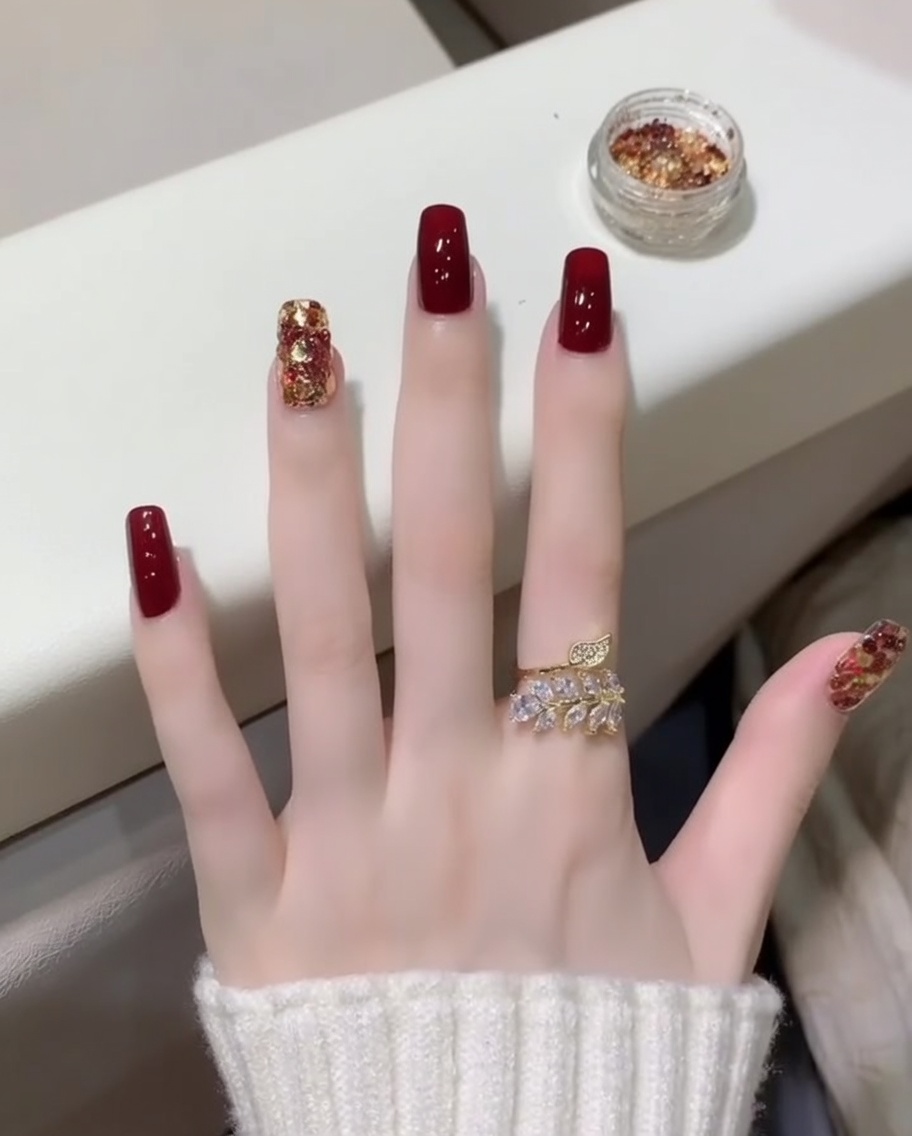 Pędzelek nakładający błyszczący top coat na paznokcie w kolorze wina i z brokatem.