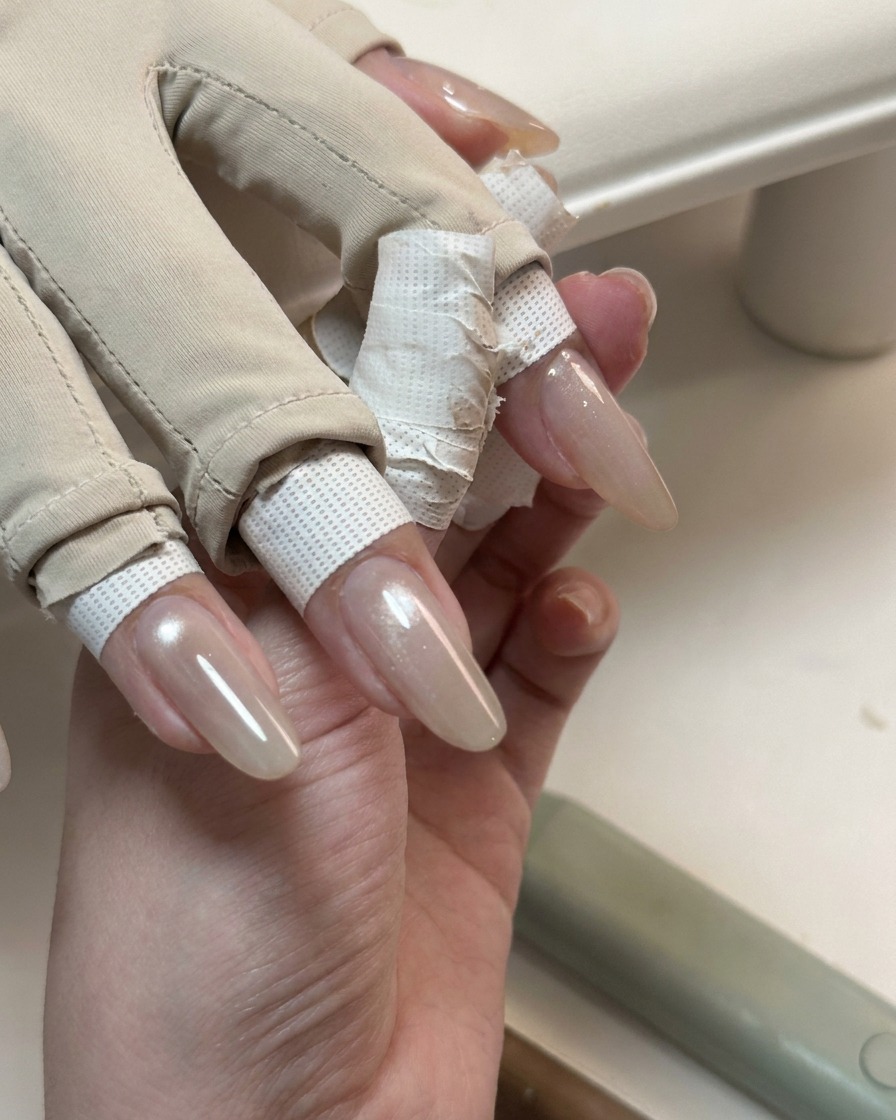 Dłoń pokazująca długie paznokcie pokryte błyszczącą, półprzezroczystą warstwą żelu cat-eye.