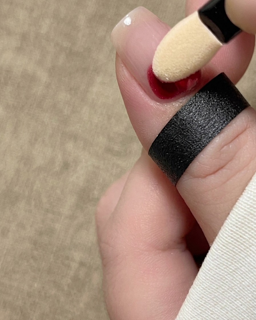 Aplikator gąbkowy do cieni wklepujący czerwony pigment u nasady naturalnego paznokcia.