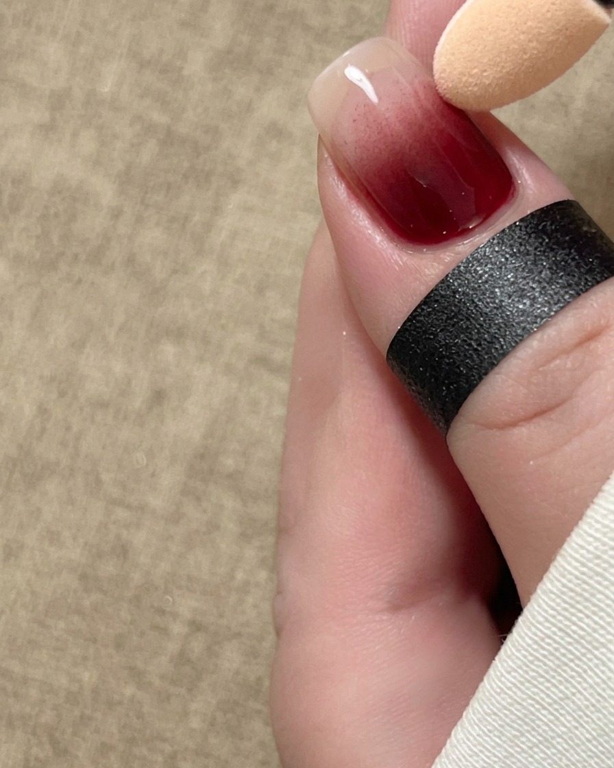 Aplikator gąbkowy miękko rozcierający czerwony pigment w formie gradientu ombre wzdłuż płytki paznokcia.