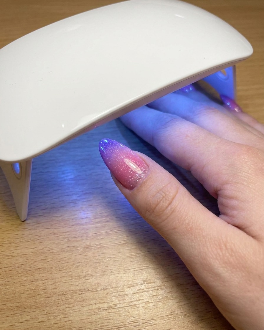 Kciuk spoczywający pod przenośną lampą UV podczas utwardzania ostatniej warstwy lakieru cat eye.