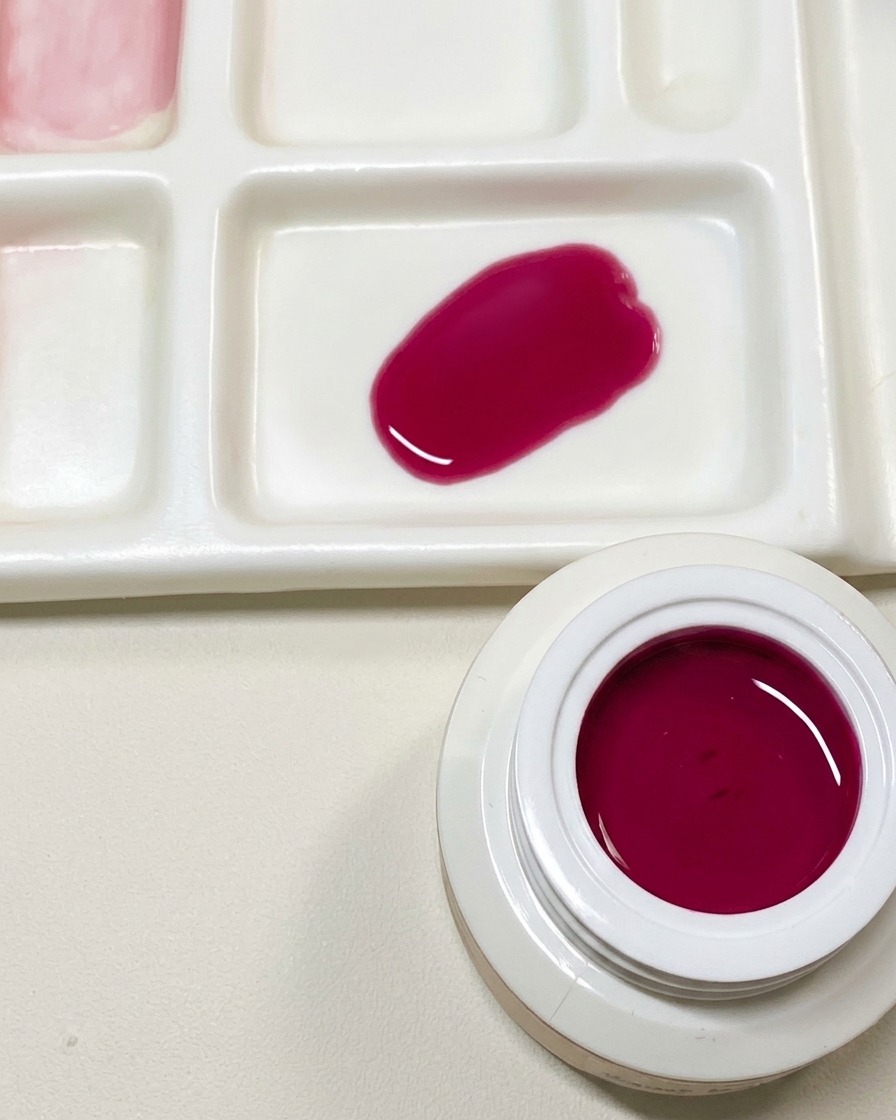 Paleta malarska pokazująca próbkę niestandardowego ciemnoróżowego żelu obok otwartego słoiczka z czerwonym żelem o smoczym owocu.