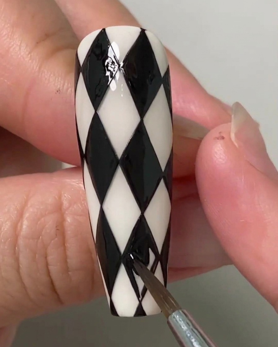 Stylistka paznokci używająca cienkiego pędzelka do wypełnienia ostatnich pozostałych rombów na czarno-białym paznokciu w stylu argyle.