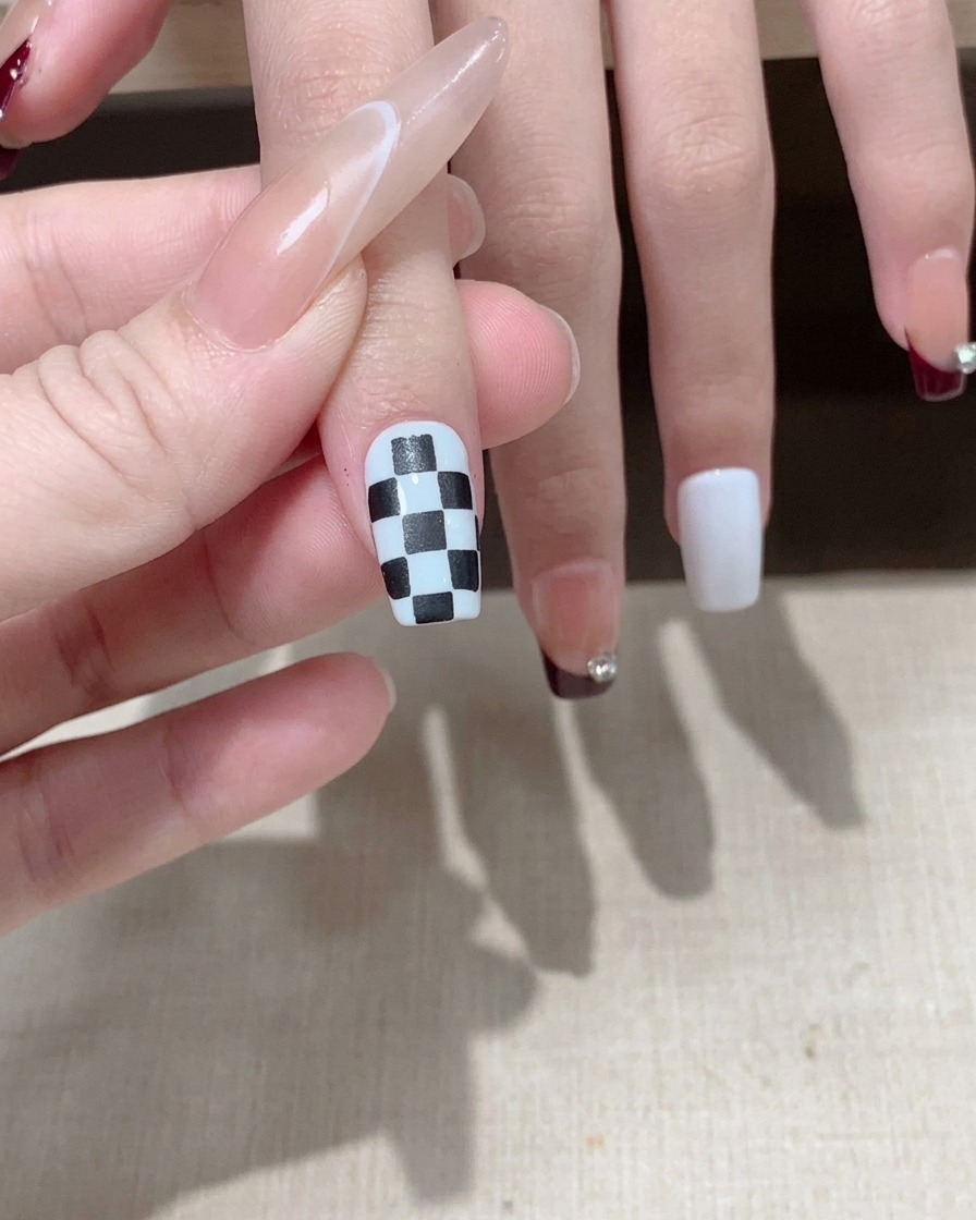 Pędzelek nakładający błyszczący top coat na gotowy wzór czarno-białej szachownicy na paznokciu.