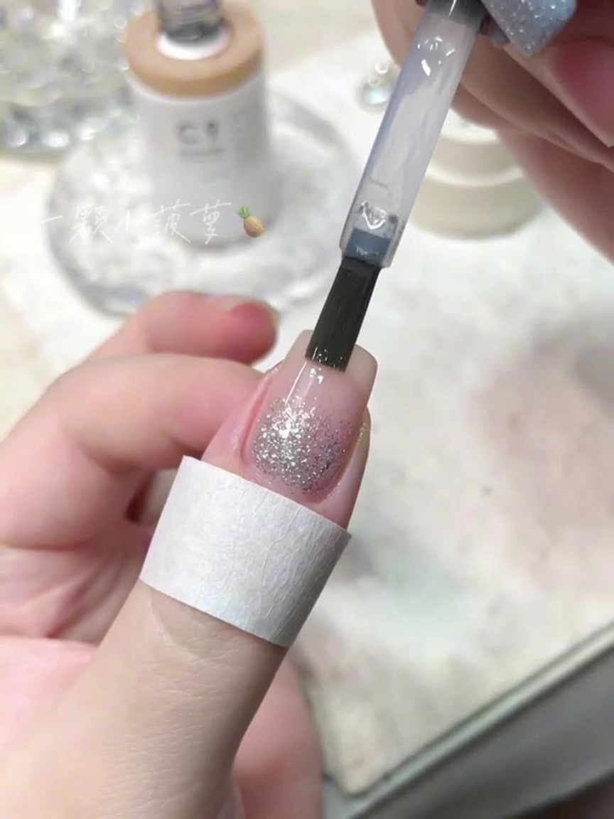 Pędzelek aplikujący bezbarwny top coat na paznokieć z brokatem.
