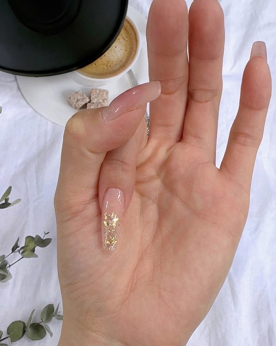 Nahaufnahme von Blattgoldflocken, die auf die feuchte Glitterschicht eines Fingernagels gedrückt werden.