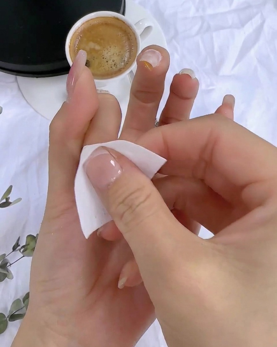 Eine Hand verwendet ein fusselfreies Pad, um die klebrige Rückstandsschicht von der ausgehärteten Nageloberfläche zu reinigen.