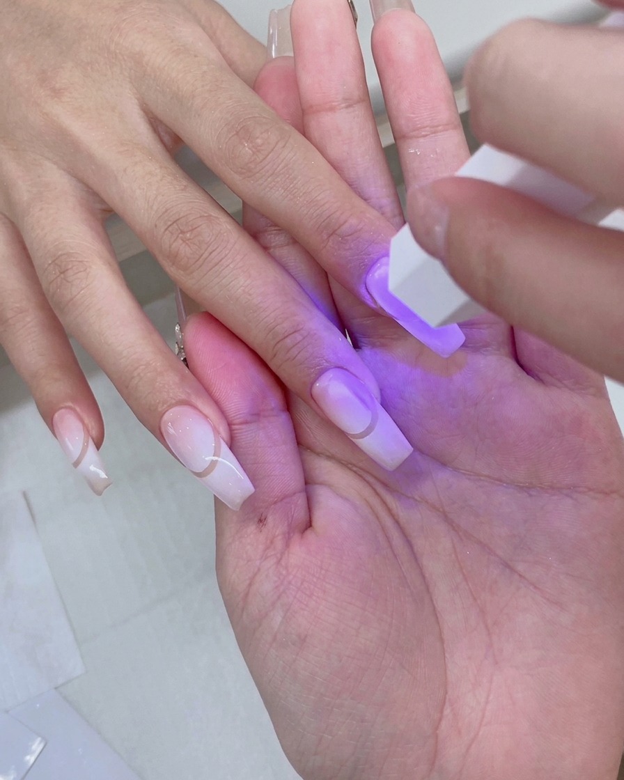 Dłoń spoczywająca wewnątrz różowej lampy UV/LED z fioletowym światłem oświetlającym przygotowane paznokcie z gradientem.