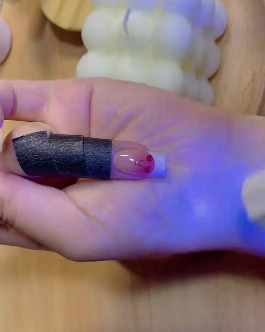Cienki pędzelek wypełniający na biało końcówkę manicure francuskiego na paznokciu z gradientem.
