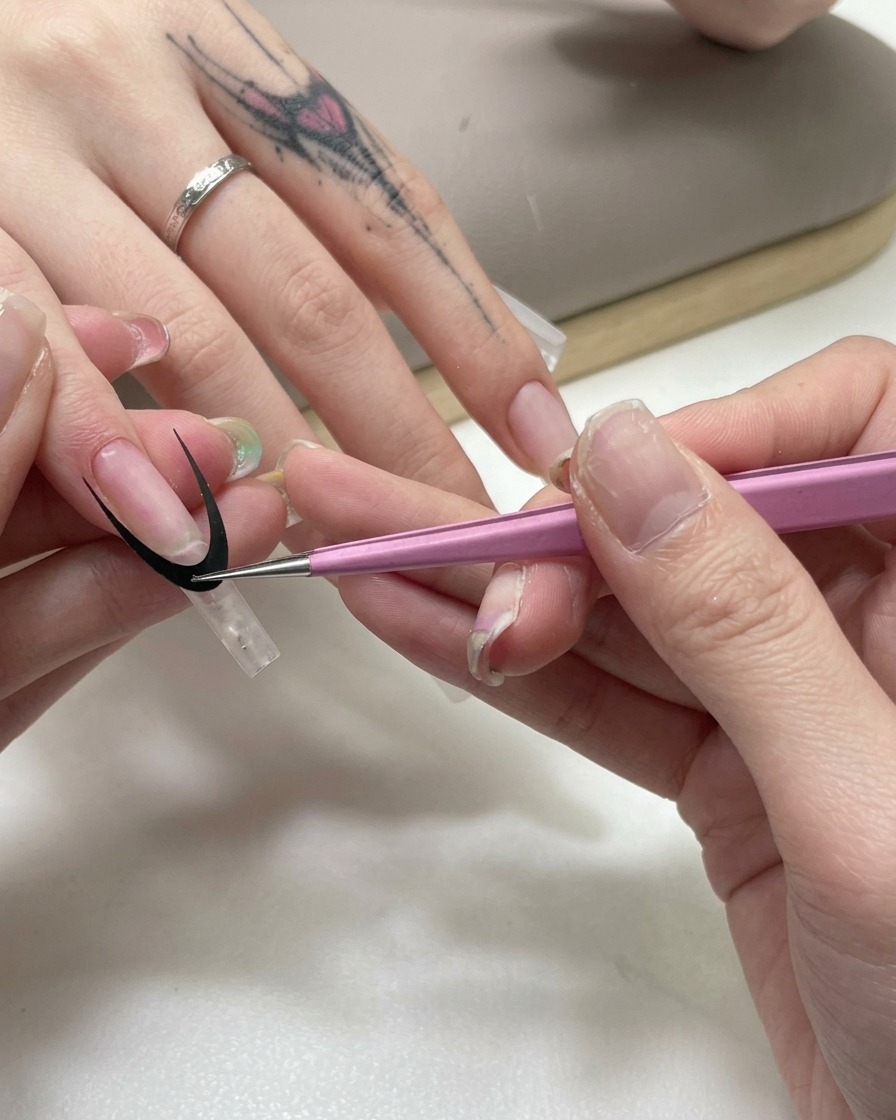 Różowa pęseta naklejająca czarną, zakrzywioną naklejkę do french manicure na przezroczyste przedłużenie paznokcia.