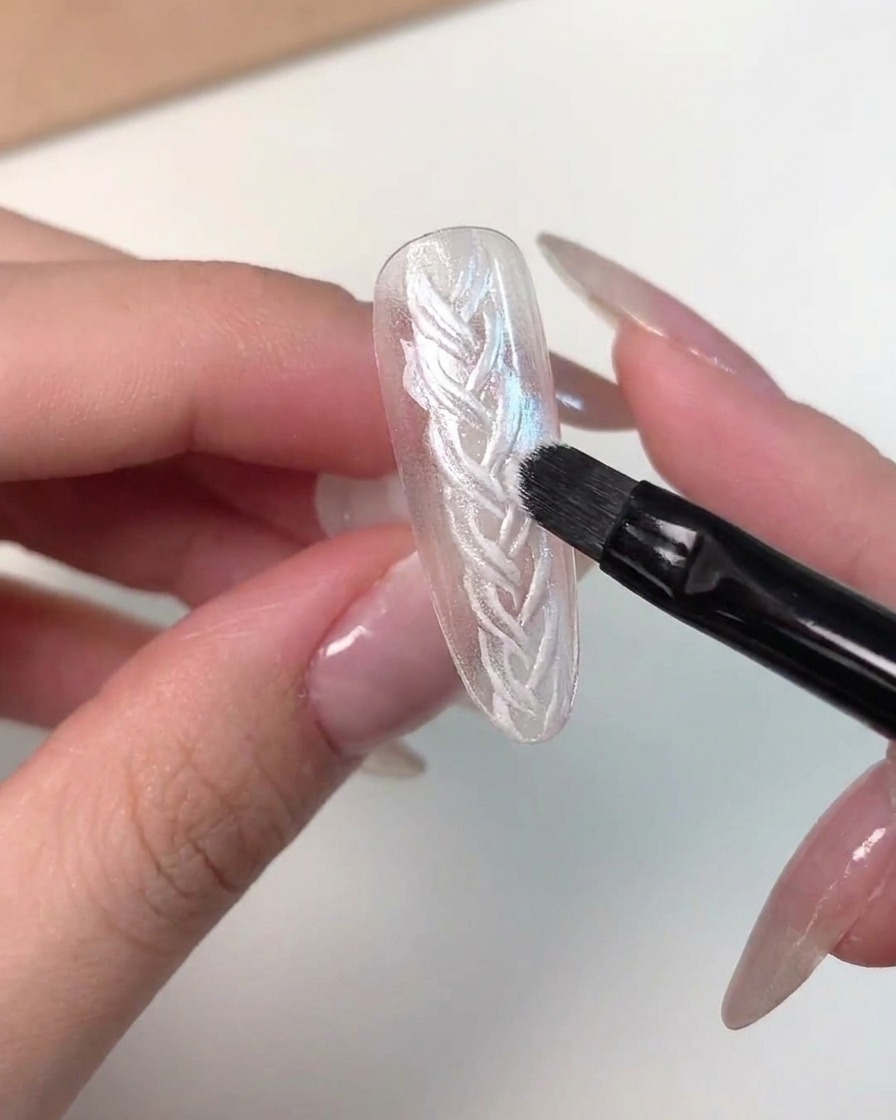 Szczegółowe zbliżenie pokazujące pędzelek nakładający różowy żel magnetyczny cat eye na tips.