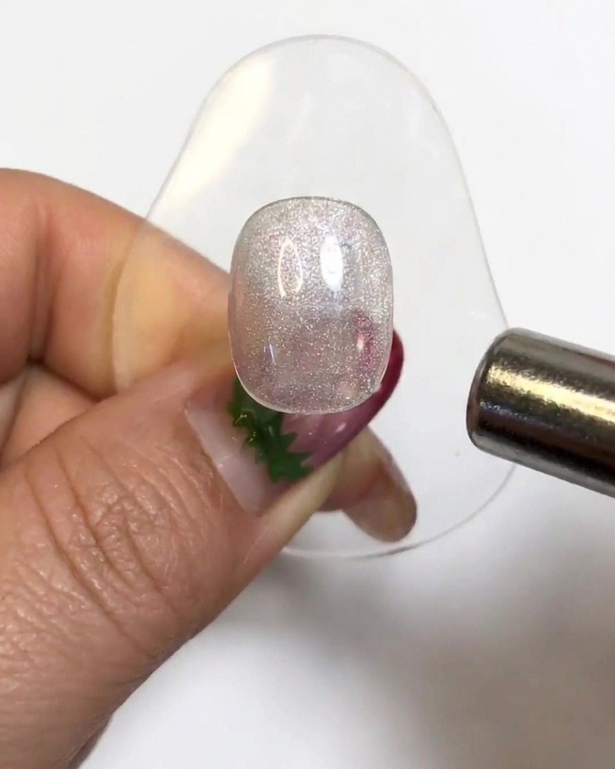 Ein zylindrischer Magnet schwebt über einem glitzernden Gel-Nagel-Tip, um die Cat-Eye-Partikel zu aktivieren.