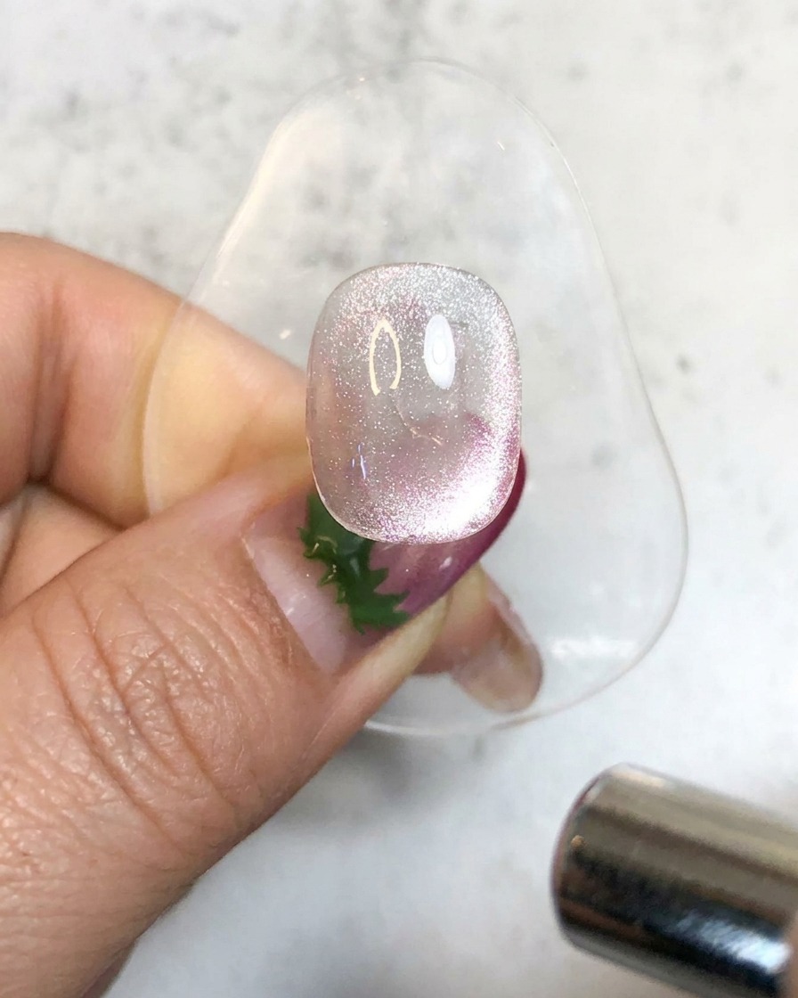 Eine Handheld-UV-Lampe beleuchtet einen glitzernden magnetischen Gel-Nagel auf einem Ständer, um ihn auszuhärten.