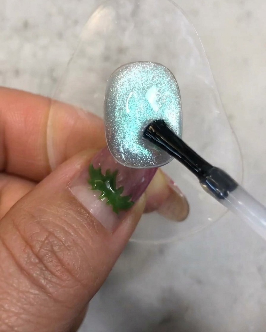 Ein Pinsel trägt einen kleinen Tropfen klaren Aufbau-Gels auf die strukturierte blaue Cat-Eye-Nageloberfläche auf.