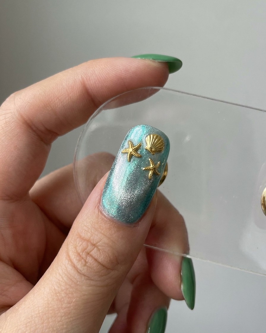 Eine Vorschau des fertigen Nagels zeigt eine blaue Cat-Eye-Basis, verziert mit goldenen Seestern- und Muschel-Charms.