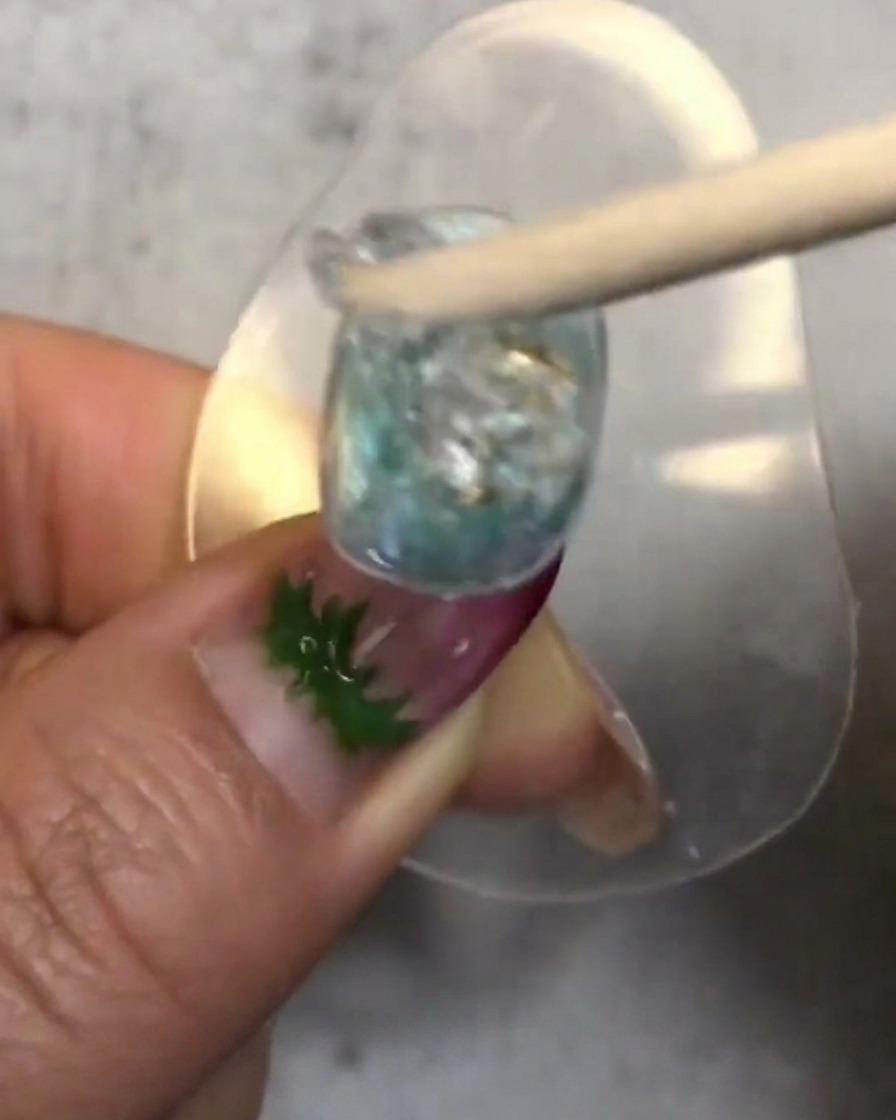 Ein Holzstäbchen rührt einen Klecks transluzentes weiches Candy-Gel um und platziert ihn auf dem verzierten Nagel.