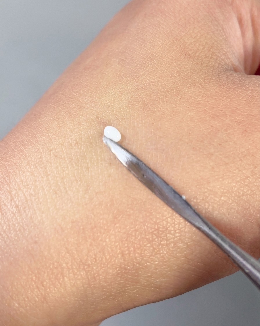 Metalowa szpatułka dociskająca małą białą kropelkę żelu 3D w gładki kształt płatka na wierzchu dłoni.