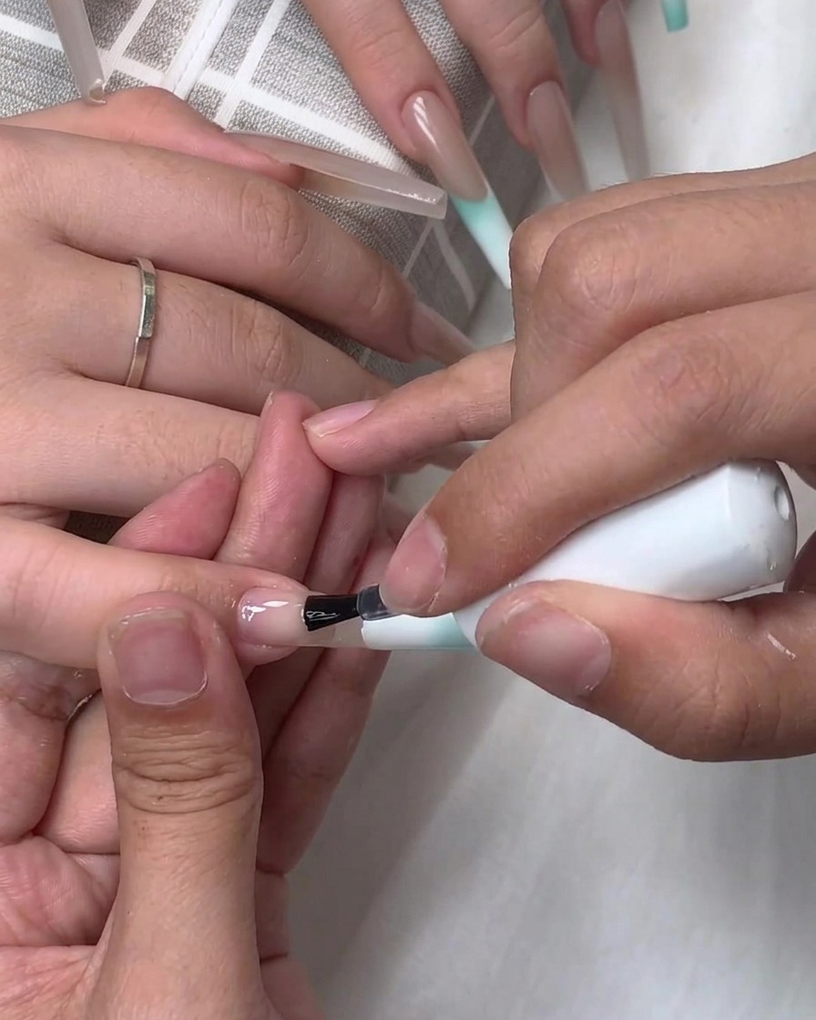 Pędzelek aplikujący bezbarwną bazę lub top coat na powierzchnię przedłużonego paznokcia.