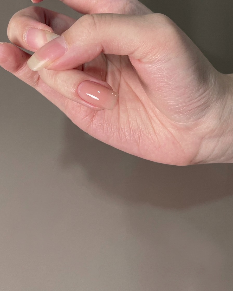 Ein Fingernagel mit einem ausgehärteten Nude Base Coat unter Beleuchtung.