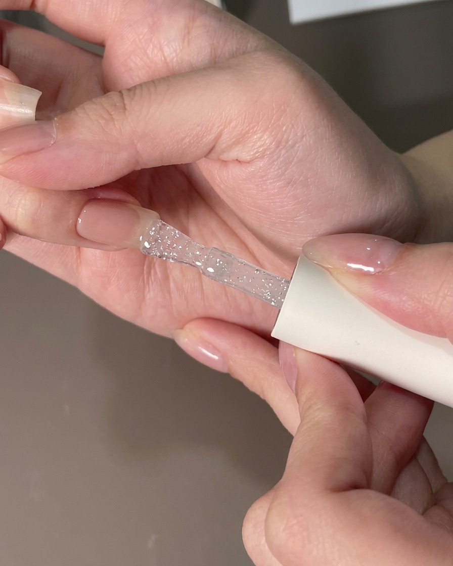 Ein flacher Pinsel glättet eine klare Gelschicht über einem Fingernagel, um Partikel zu entfernen.