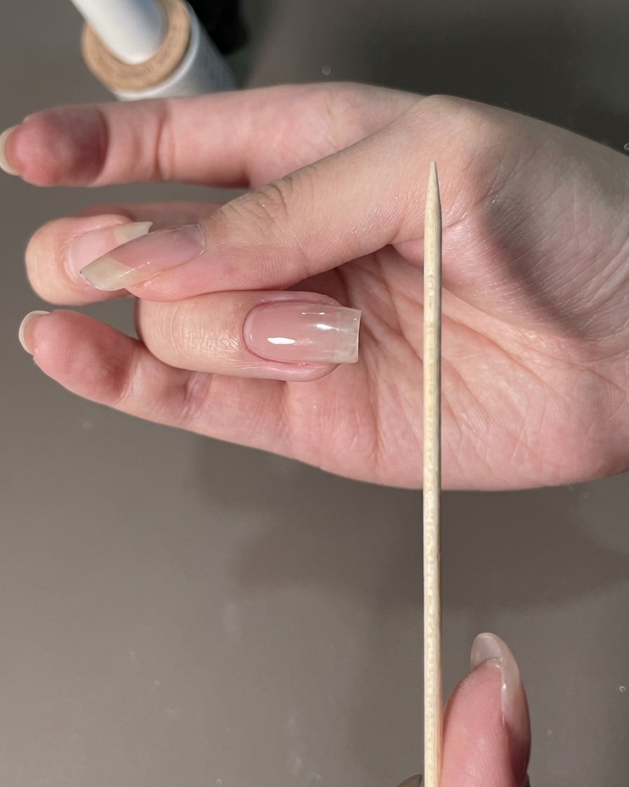 Eine Nagelfeile wird neben eine manikürte Hand gehalten, um die Nagelränder zu formen.