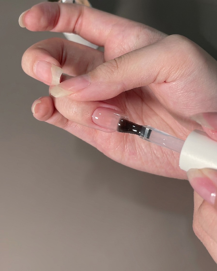 Ein Pinsel trägt einen Top-Coat-Versiegeler auf einen mit Chrompuder veredelten Nagel auf.